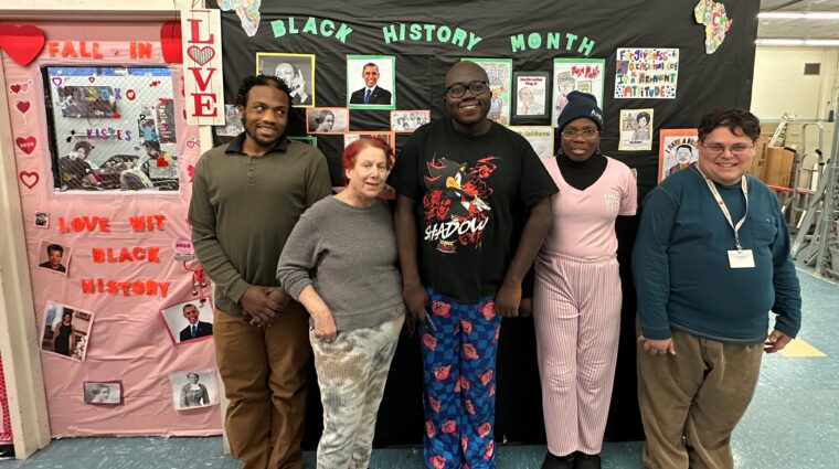 Five people supported by AHRC Nassau stand in front of a display for Black History Month