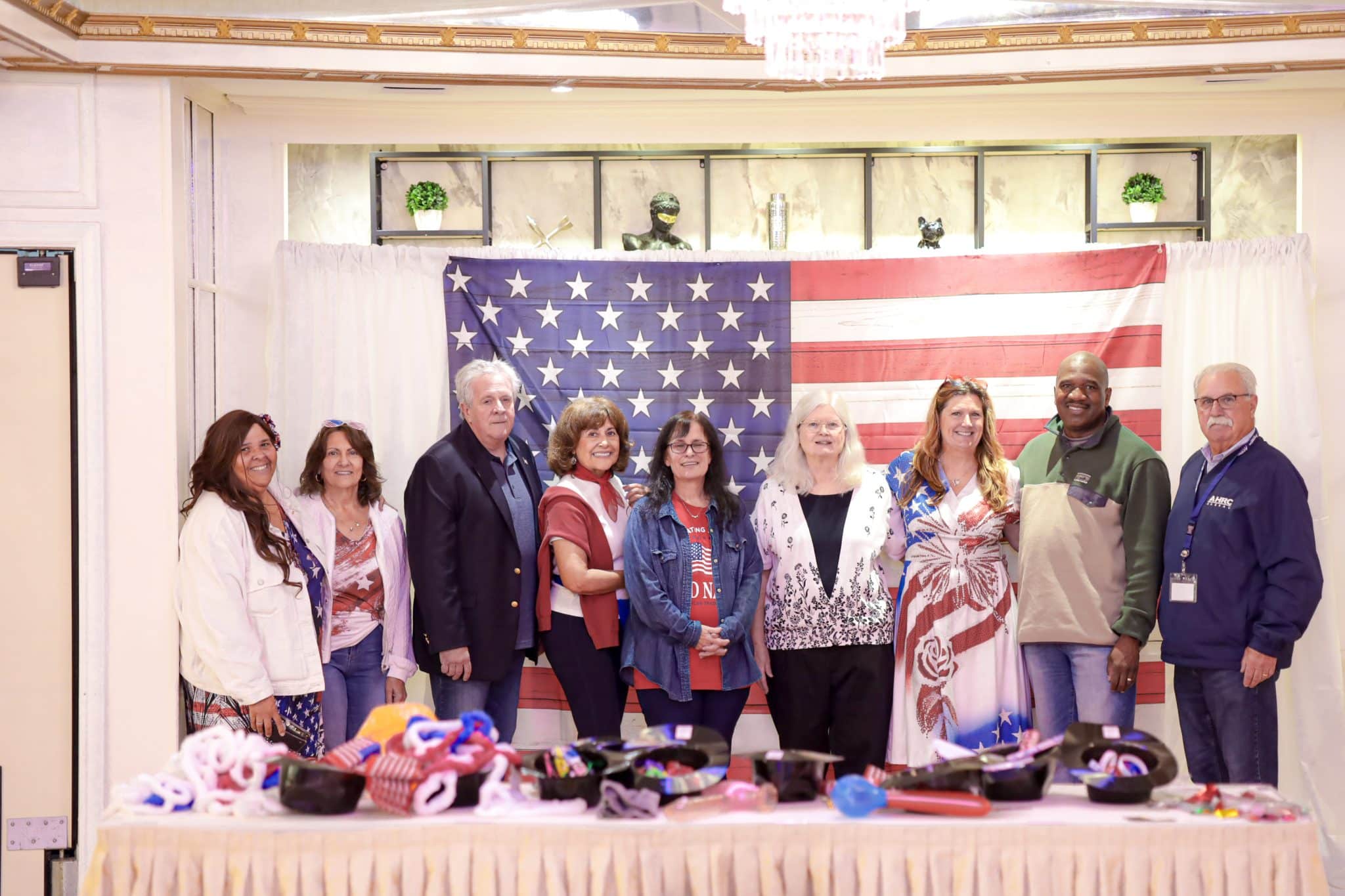 Nine AHRC Nassau employees stand in front of a large poster of the American flag at the guardianship party