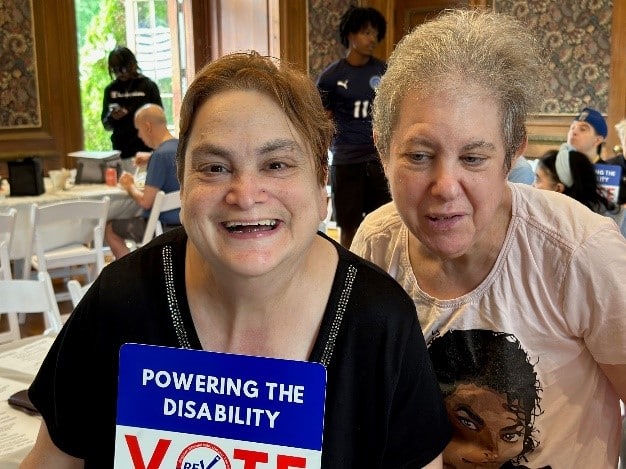 Self-advocates pose with a sign that reads "Powering the disability - VOTE" at the Voter Demonstration rally